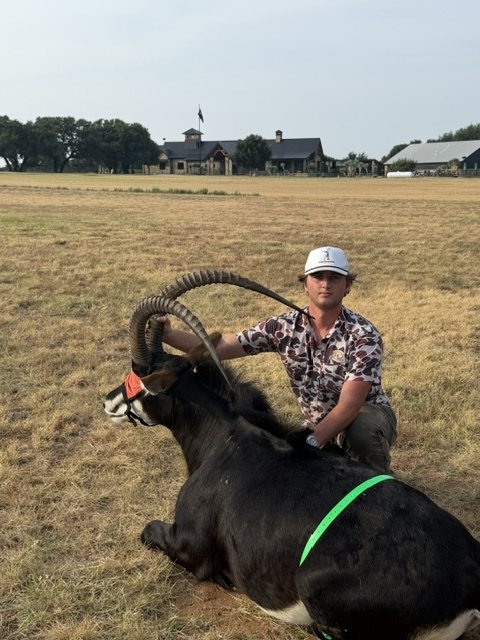 One of the brothers kneeling with a sable antelope in a pasture